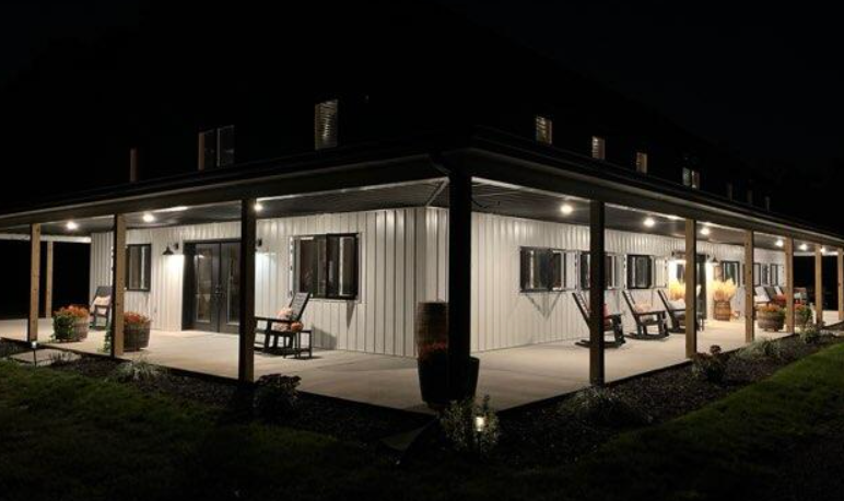 Night exterior view of a two-story white building with a wrap-around porch with rocking chairs visible.