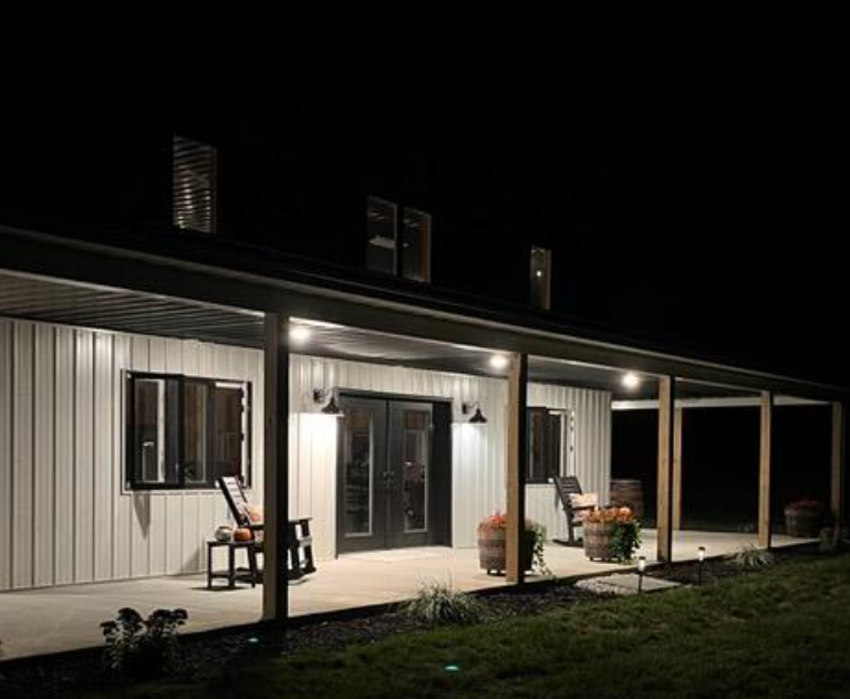 A modern home at night with a covered porch, lit by overhead lights.