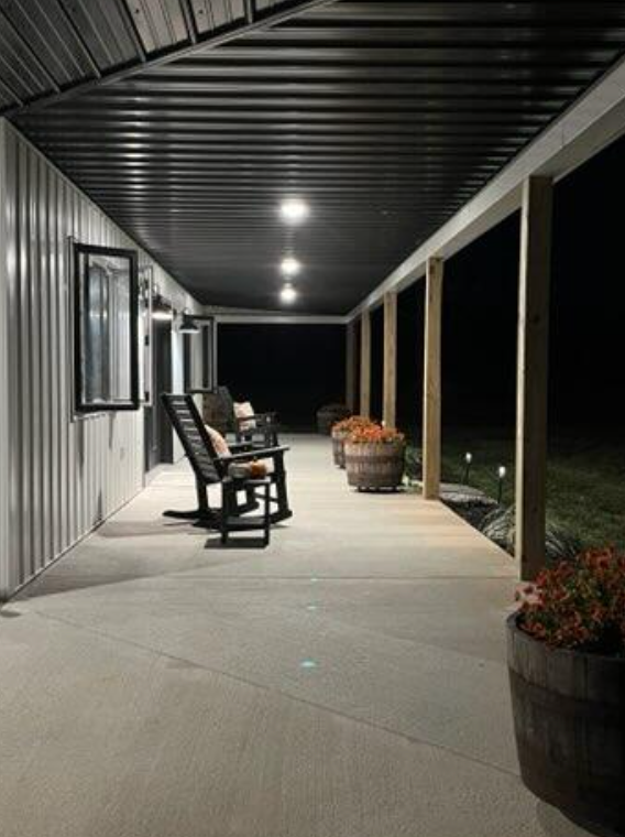 Covered porch at night with chairs, potted plants, and overhead lights and shows full view of metal ceiling.