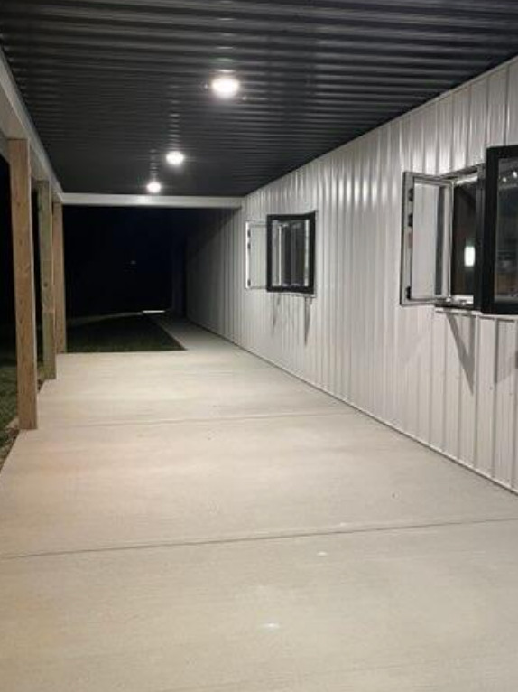 Covered concrete porch with white metal siding, windows, and a dark corrugated ceiling.