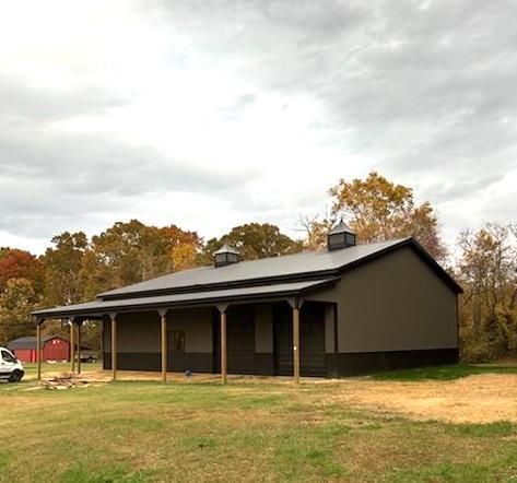 A large barn with a porch is sitting in the middle of a grassy field.