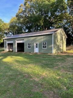 A green garage with a brown roof is sitting in the middle of a grassy field.