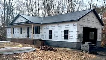 A house is being built in the woods with a black metal roof.
