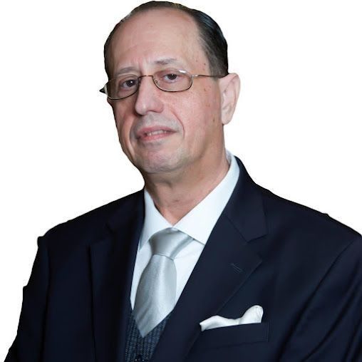 Man in suit and tie, wearing glasses, looking forward with a neutral expression.