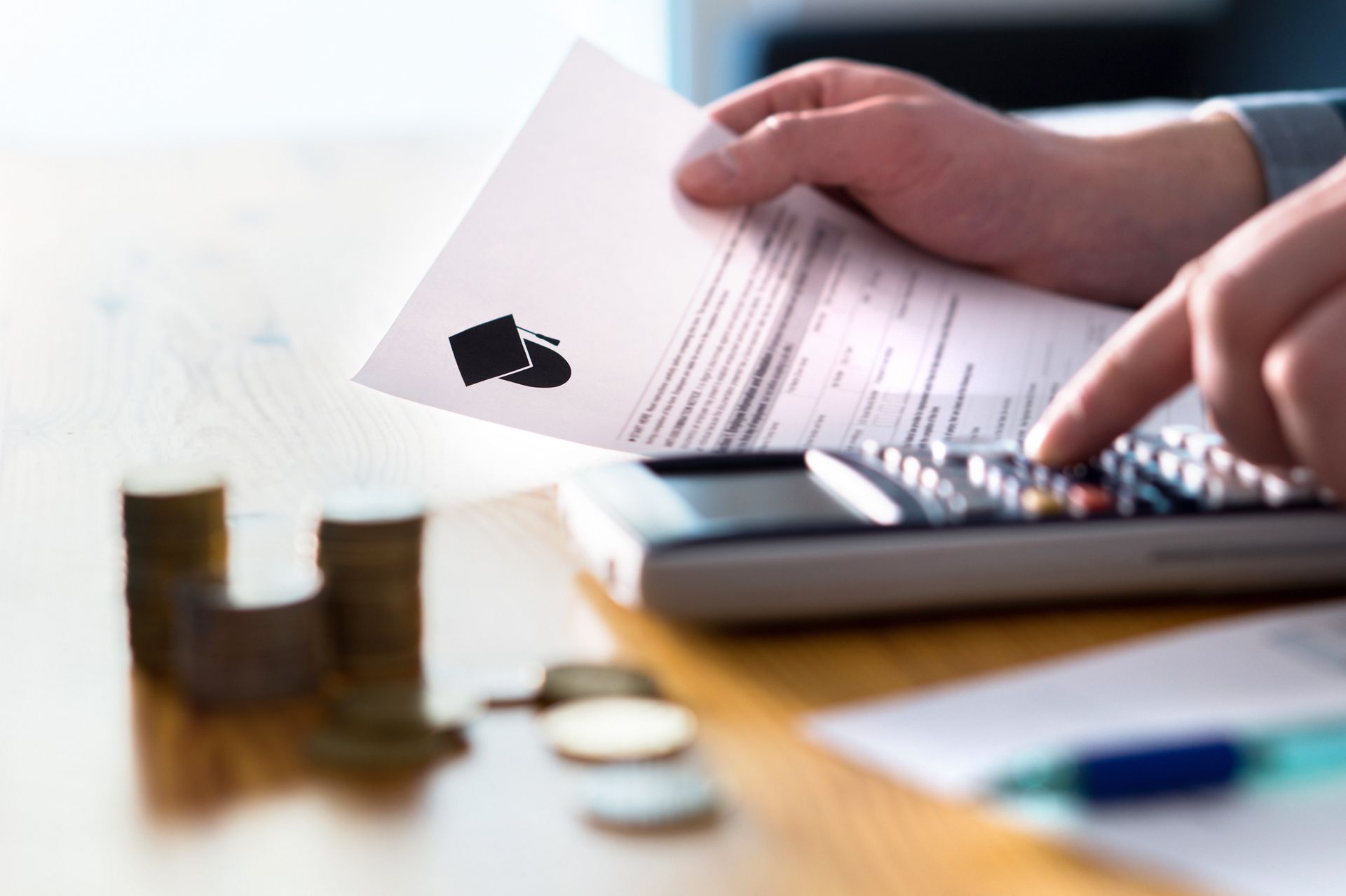 Hands calculating expenses with a calculator, document and coins on a table.