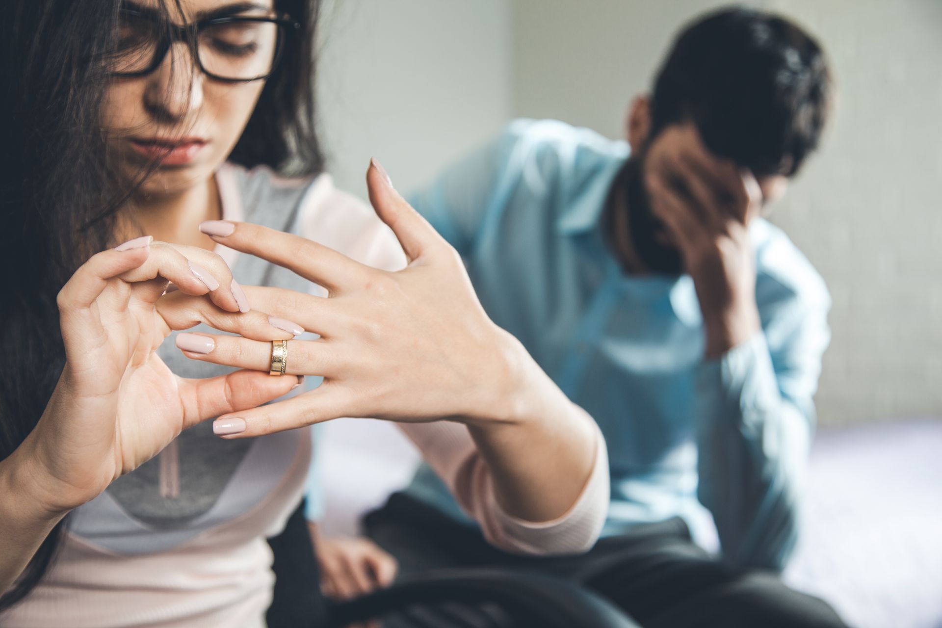 Person's hands removing a diamond ring from finger; white blouse in background.