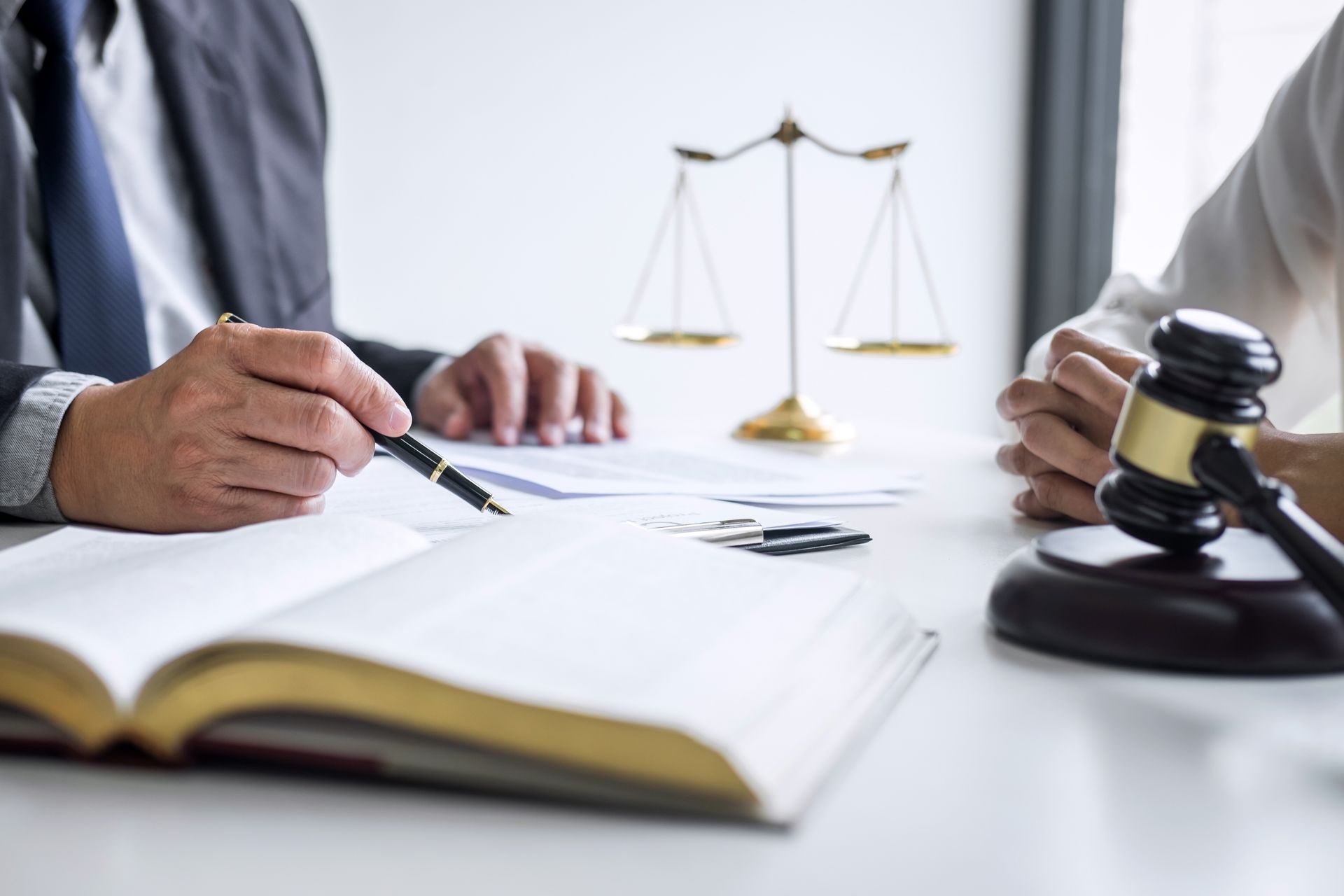 Lawyer points to document, discussing with a client at a table with scales and gavel.