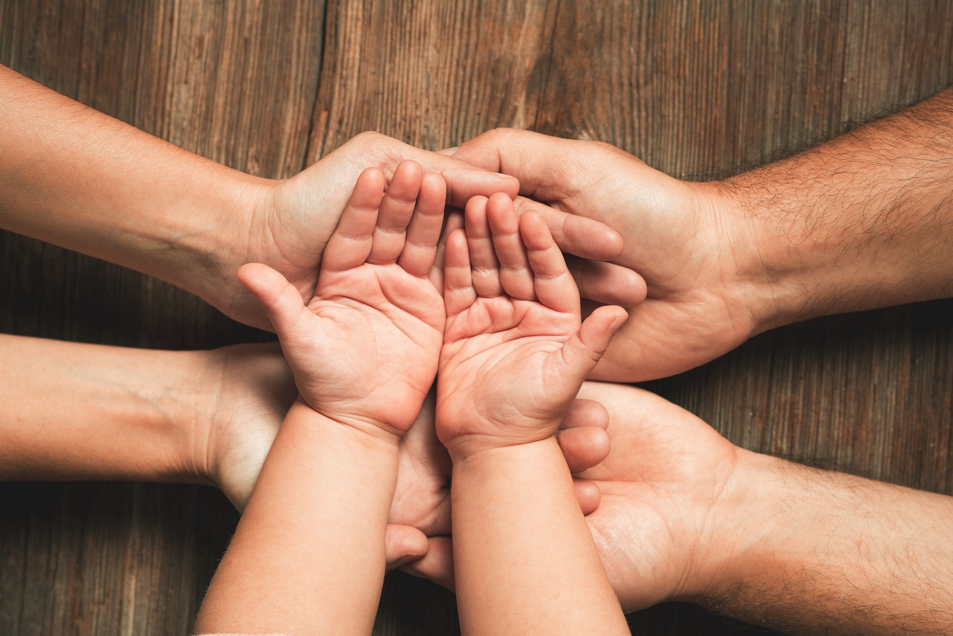 Four hands, of varying sizes, stacked on top of each other, on a wooden surface.