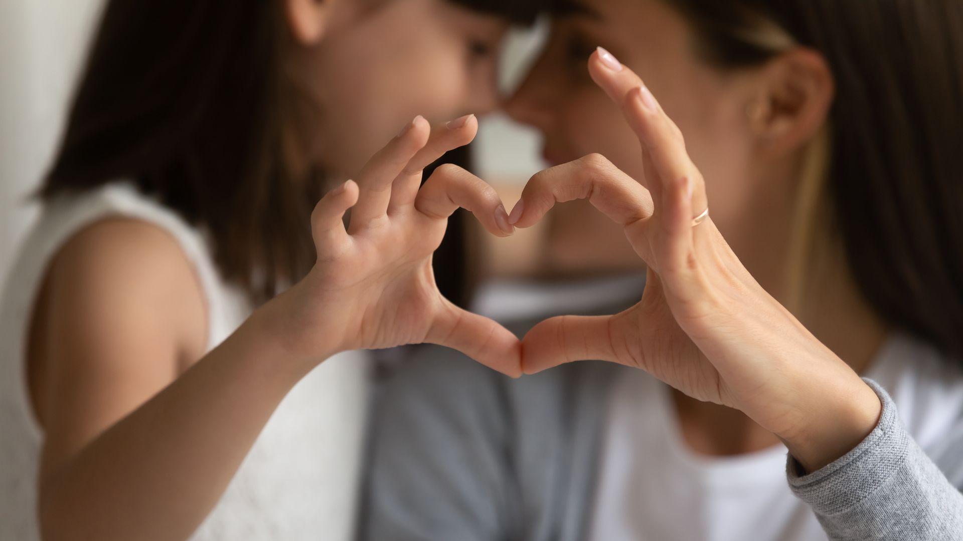 Mother and child forming a heart shape with their hands, close together.