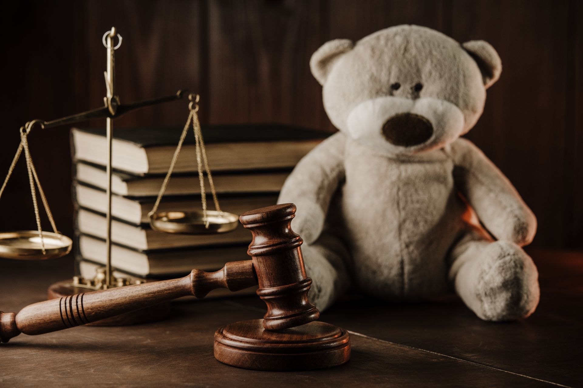 Teddy bear, gavel, scales of justice, and books on a dark wooden surface.