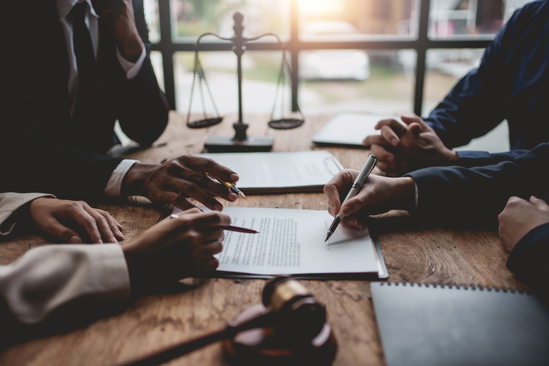 People in a meeting signing papers around a wooden table in a bright office People in a meeting signing papers around a wooden table in a bright office