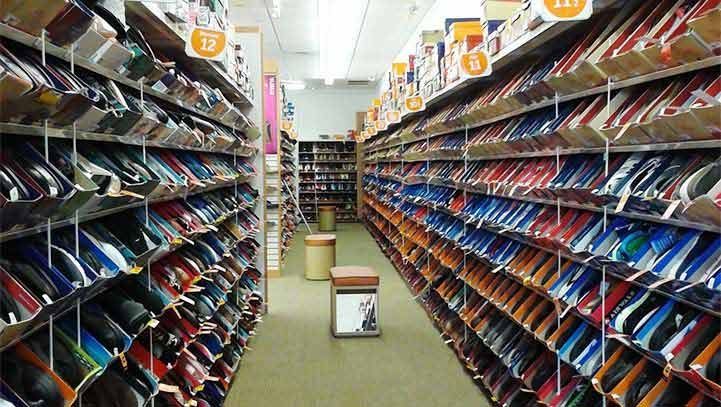 Rows of shoes on shelves in a shoe store aisle.