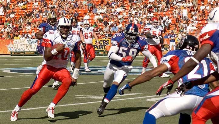 Football player in red and white uniform runs with the ball toward the end zone, pursued by a player in blue.