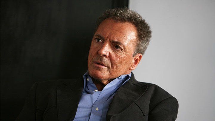 Man in a suit jacket and blue shirt, looking to the side with a contemplative expression.