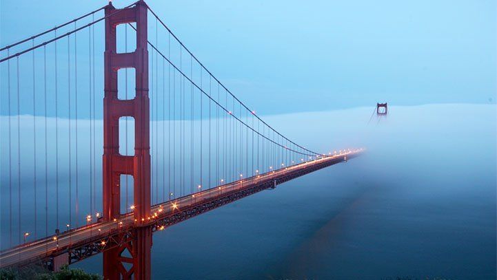 Golden Gate Bridge in San Francisco partially obscured by fog, illuminated at dusk, orange and red.