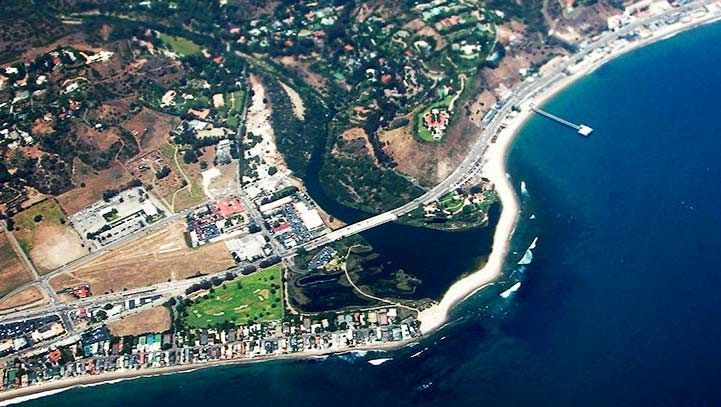 Aerial view of Malibu, California coastline: ocean, beach, highway, bridge, buildings, and a lagoon.