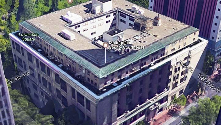 An aerial view of a multi-story square building in an urban setting.