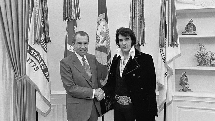 President Nixon shakes hands with Elvis Presley in the Oval Office, surrounded by flags.