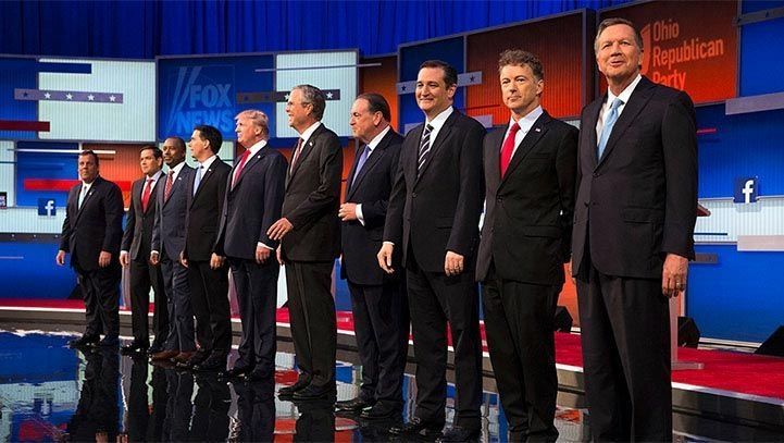 Republican presidential candidates on a stage, suited, facing forward, under bright lights. Fox News logo visible.