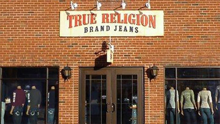 True Religion store exterior with sign above the double doors, mannequins in windows. Red brick building.