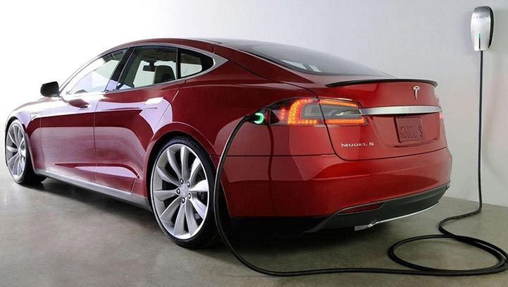 Red Tesla Model S electric car charging from a wall outlet.