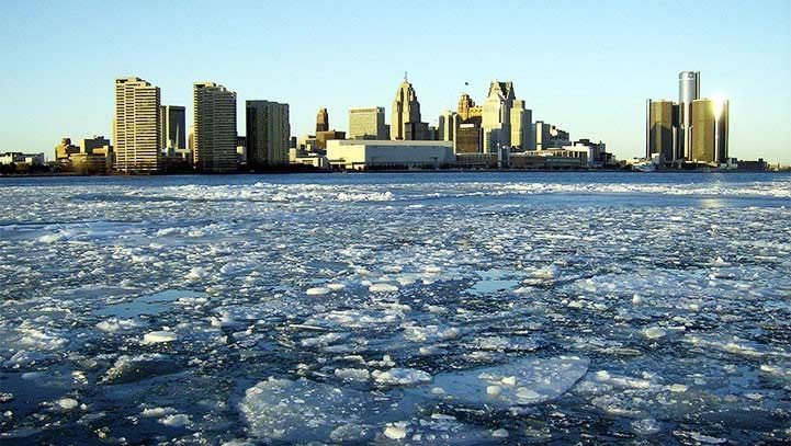 Detroit skyline across a frozen river. Ice chunks float in the water; clear sky overhead.