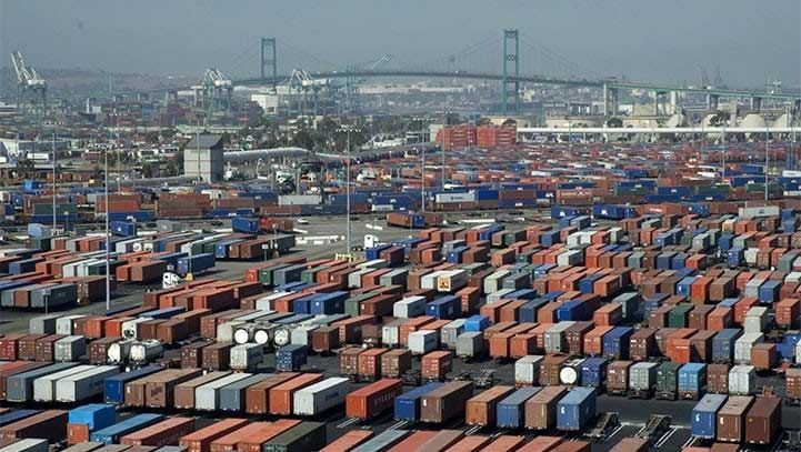 A large port with numerous shipping containers in rows; bridge in the background.