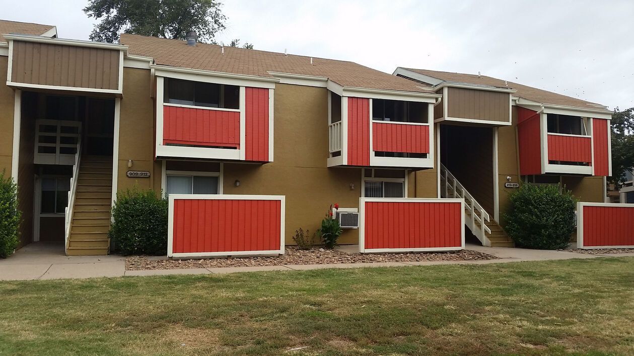 Apartment building with orange accents, tan exterior, and a brown roof.