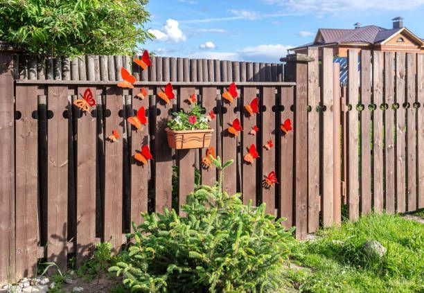 A decorative wooden fence with a bush growing in front and a plant pot, below paper butterflies.