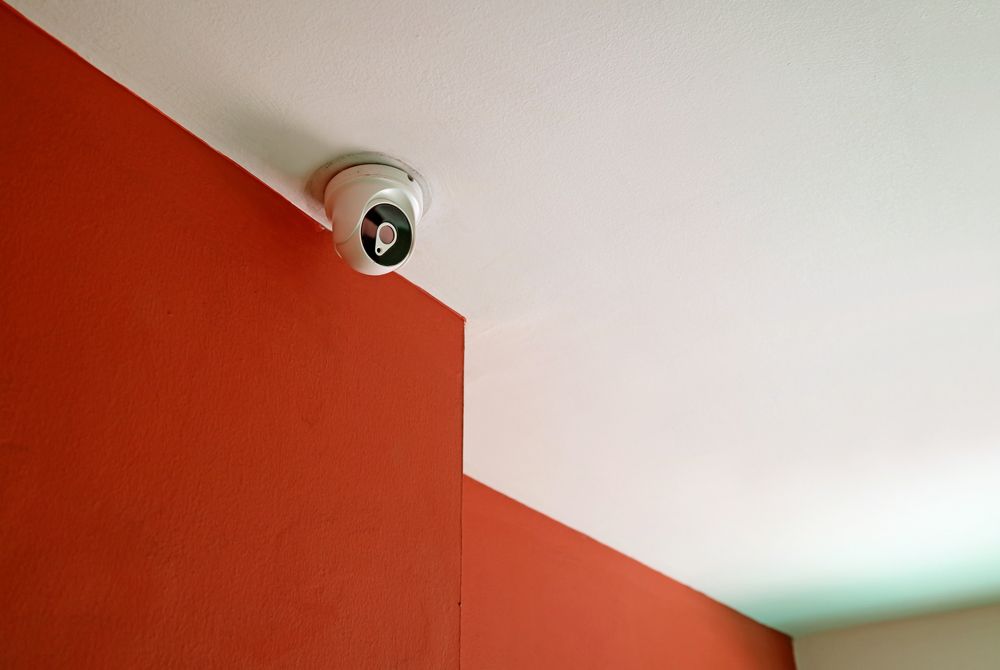 A Security Camera is Mounted on the Ceiling of a Room Next to a Red Wall — Direct Connect Services In Buderim, QLD