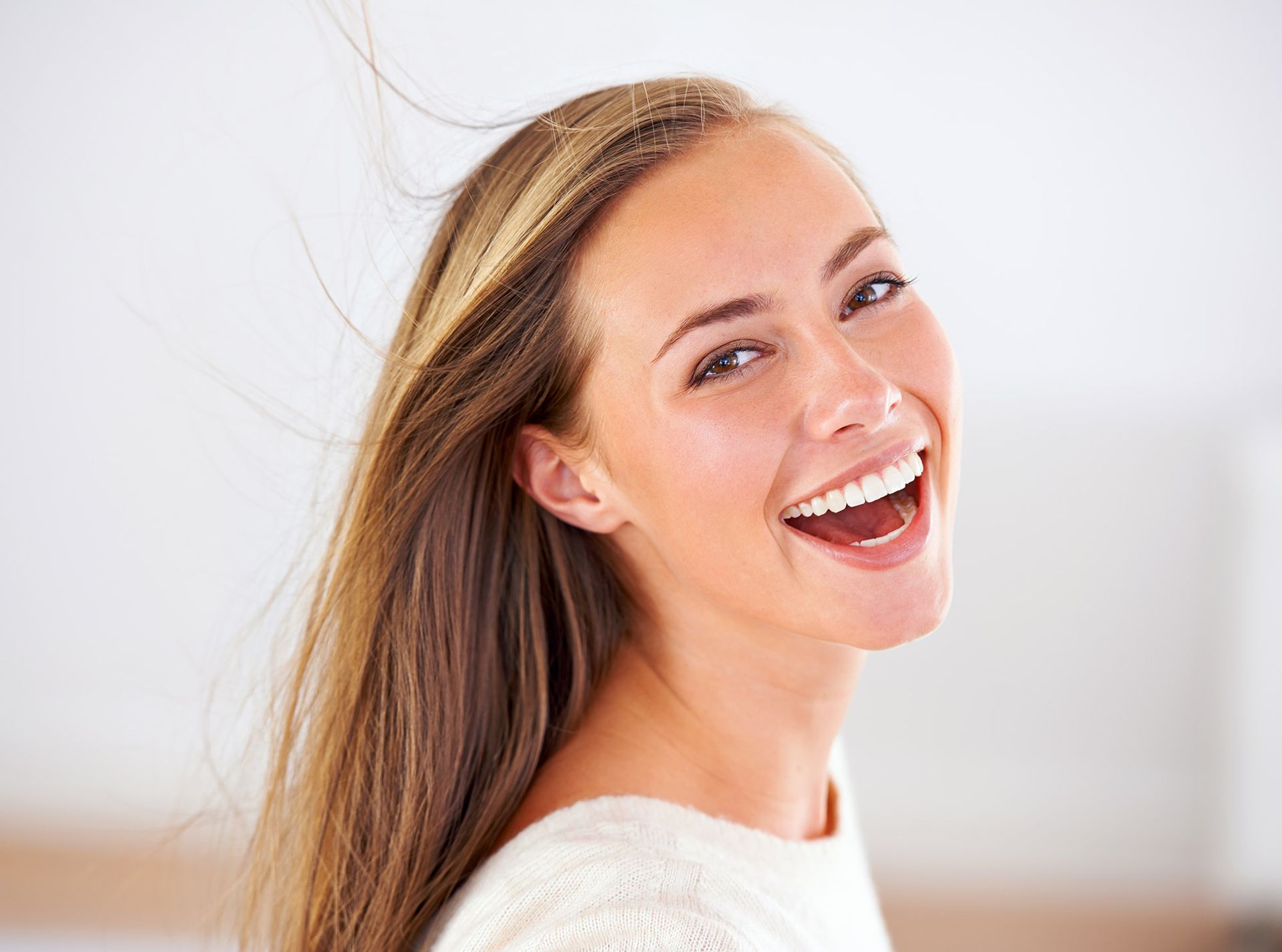 Woman with long brown hair smiles widely, looking toward the viewer.
