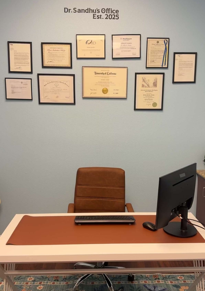 Office desk with a computer and chair, diplomas on a blue wall.