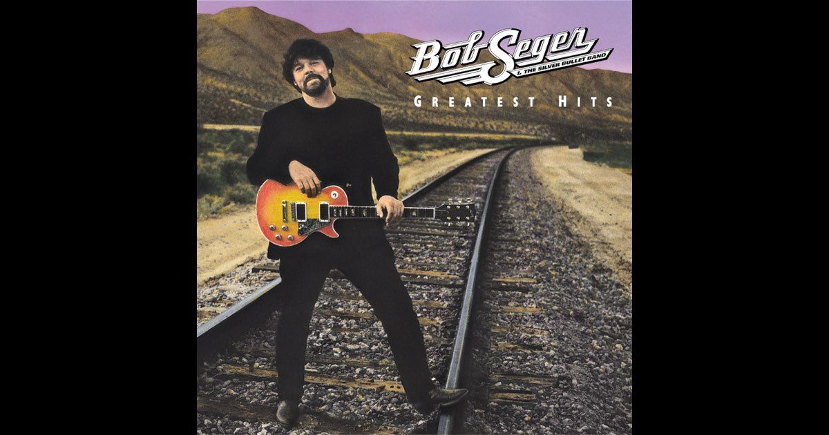 Bob Seger stands on train tracks, holding a guitar, on the