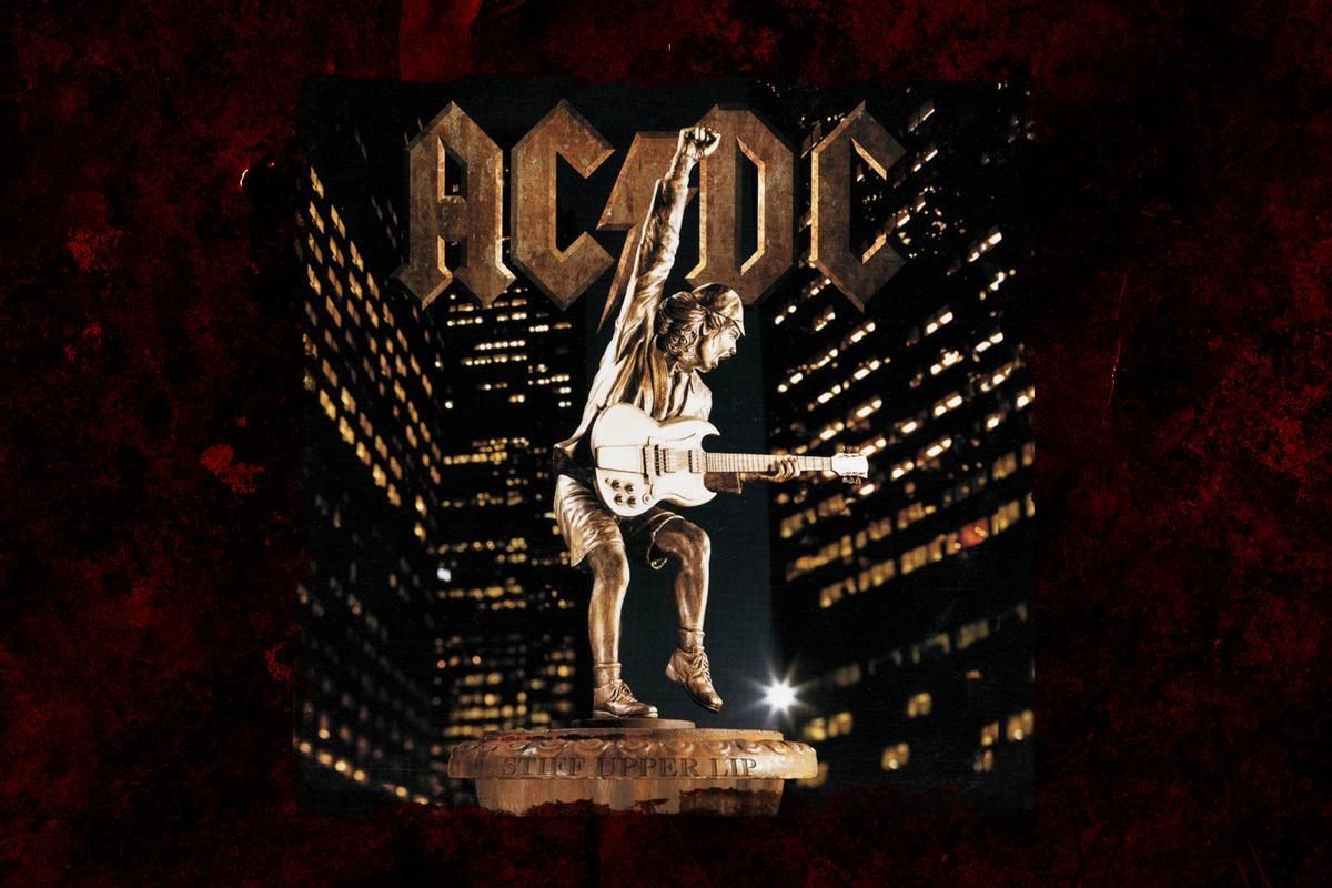 AC/DC album cover: Statue of a guitarist atop a building with the band's logo above, night city backdrop.
