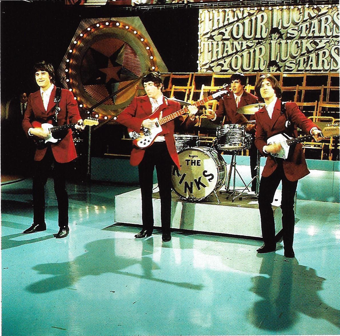 The Kinks on a stage, red jackets, black pants, vintage drum kit.