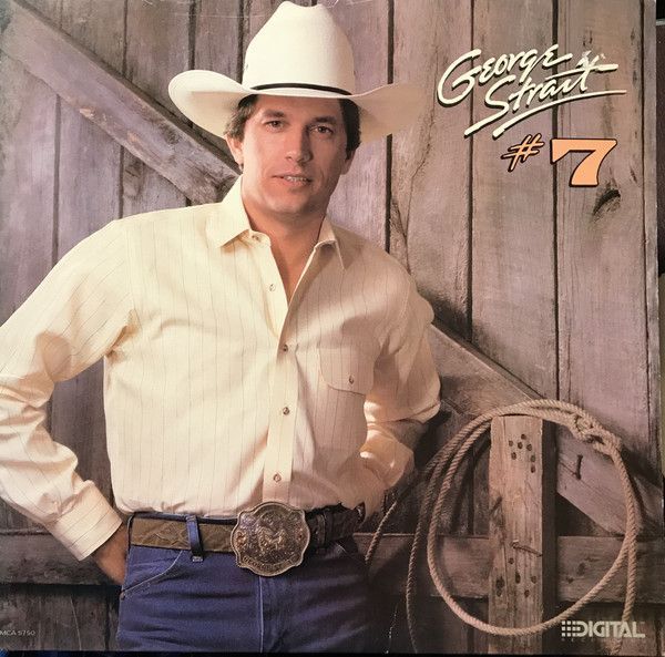 George Strait leaning against a wooden door, wearing a cowboy hat, shirt, jeans, and belt buckle, with a lasso nearby.