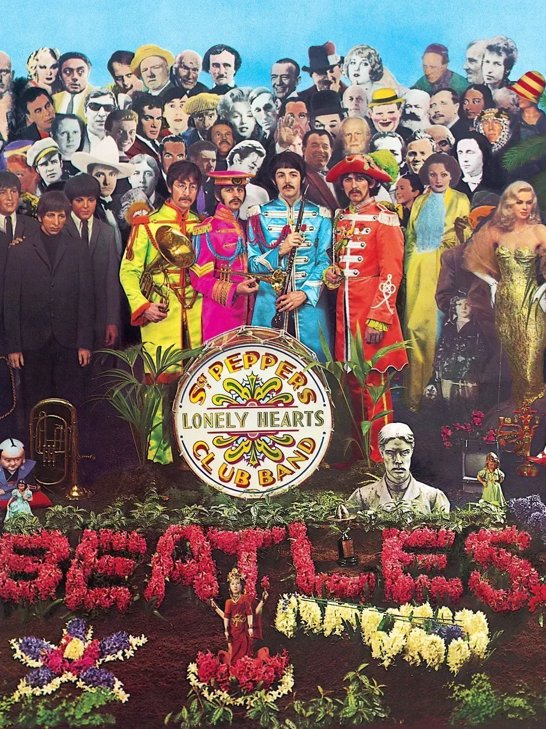 The Beatles in colorful uniforms stand with a crowd of famous faces. A floral arrangement spells