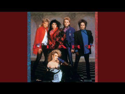 Heart band members posing for an album cover, featuring two women and three men in colorful outfits, set against a dark background.