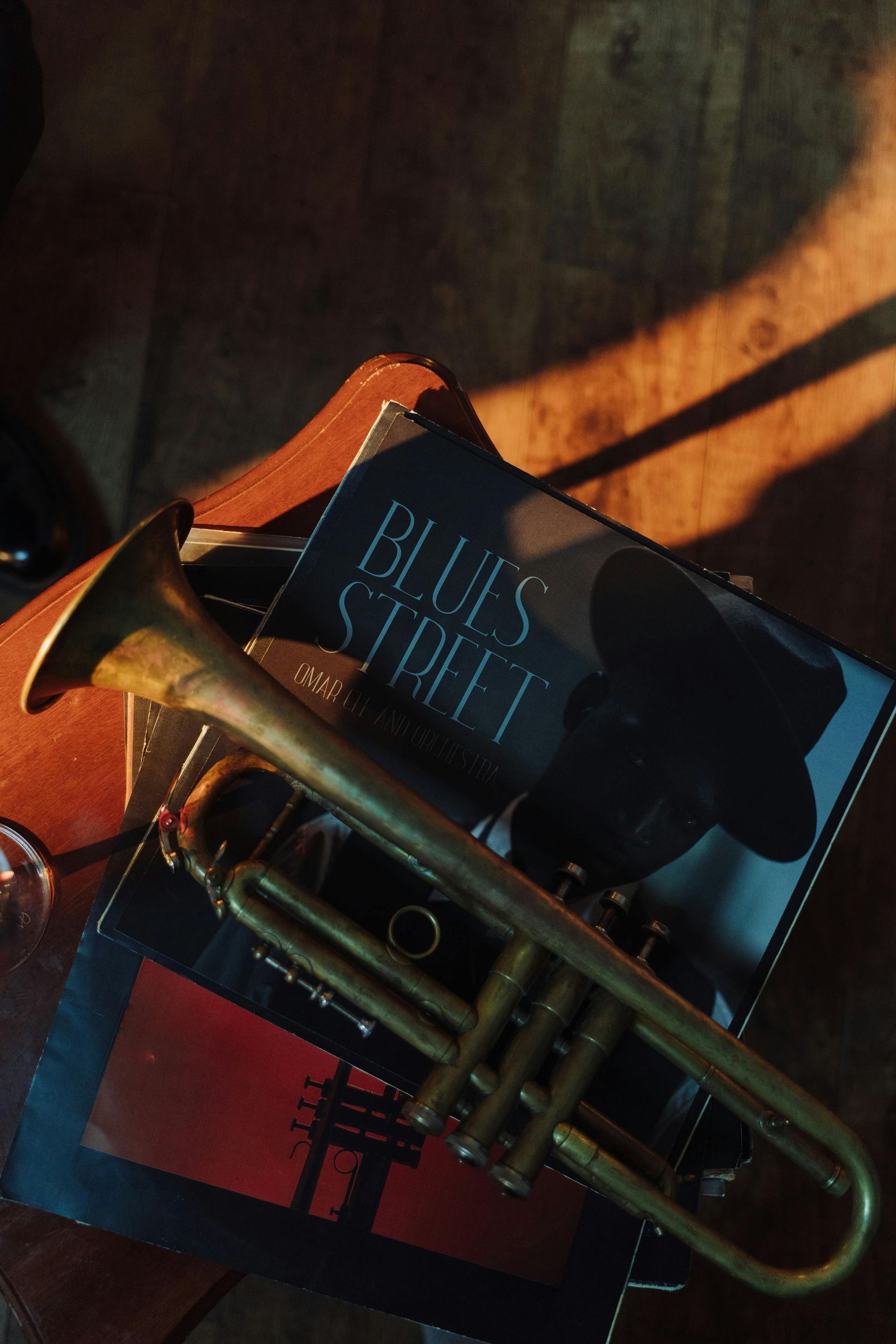 Silhouette of a person playing a saxophone against an orange and blue sunset, wearing a hat.