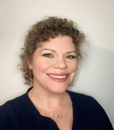 Smiling person with curly hair wearing a dark top against a light background