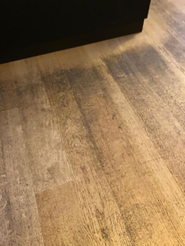 Een close-up van een houten vloer met een zwarte kast op de achtergrond.