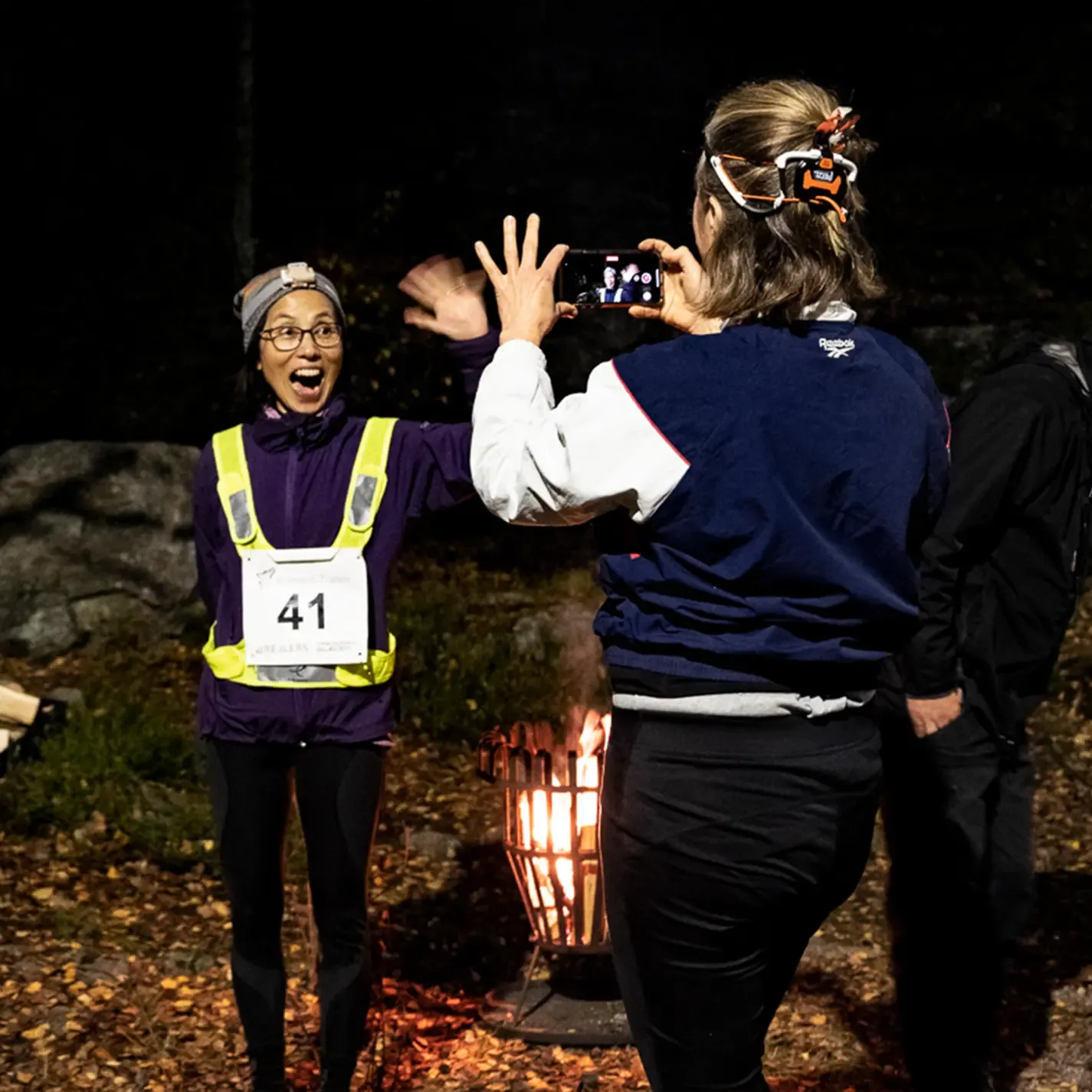 A woman taking a picture of another woman wearing a number 41 bib