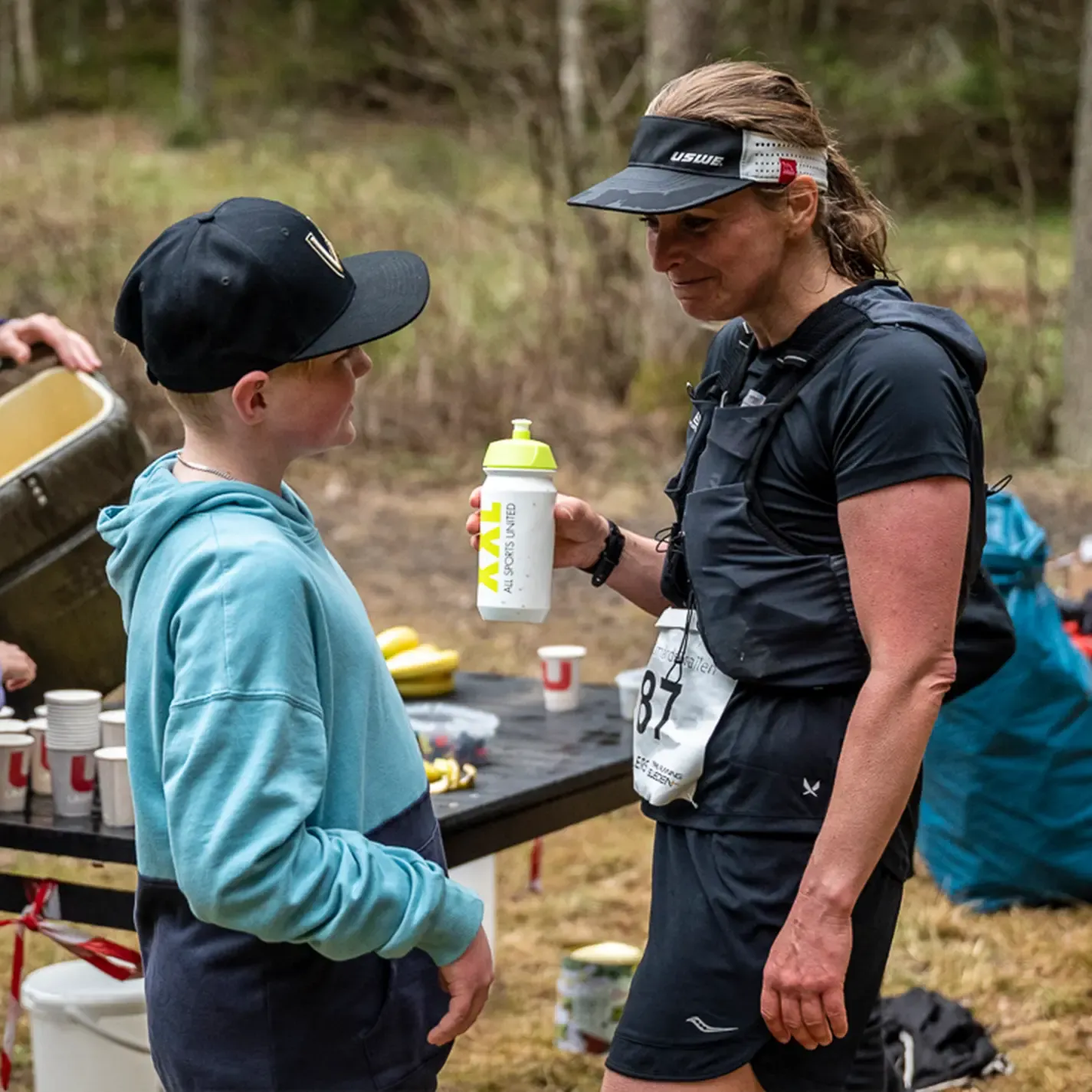A woman is holding a water bottle and talking to a boy.