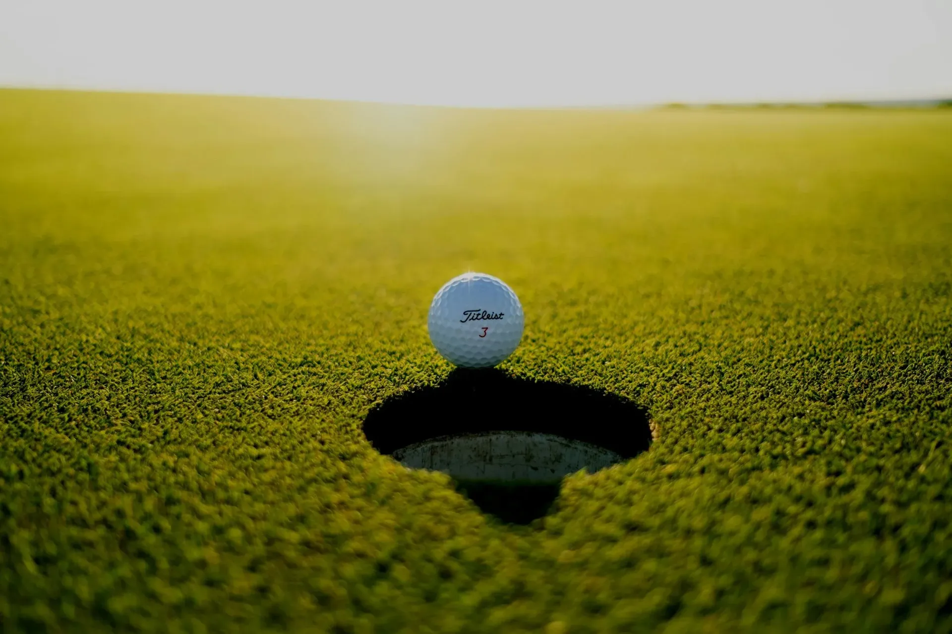 Ein Golfball schwebt über einem Loch auf einem grünen Putting Green, der Hintergrund ist verschwommen.