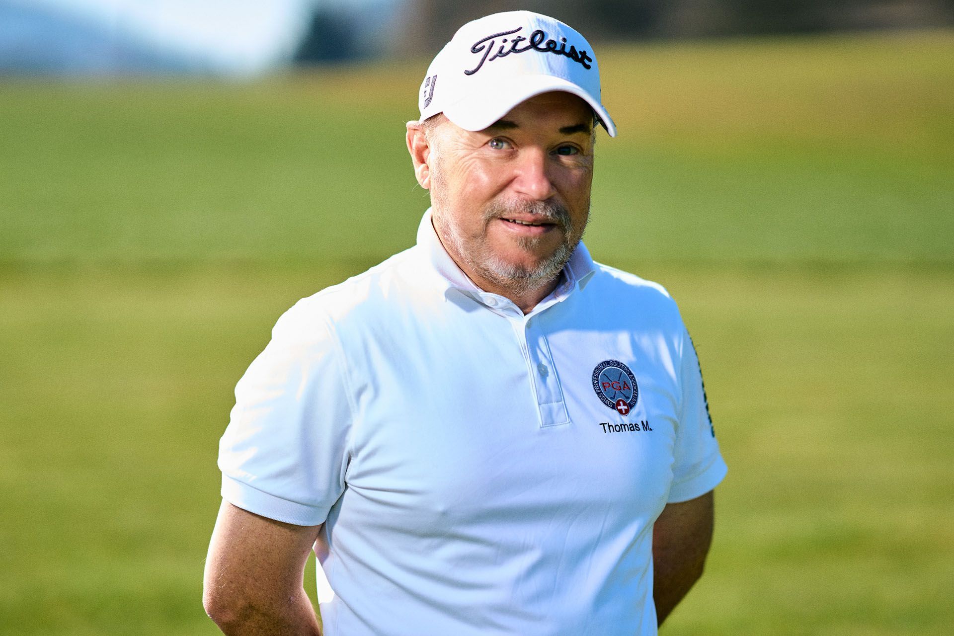 Thomas Mondani weißem Polohemd und Kappe steht auf einem grünen Golfplatz und blickt zur Seite