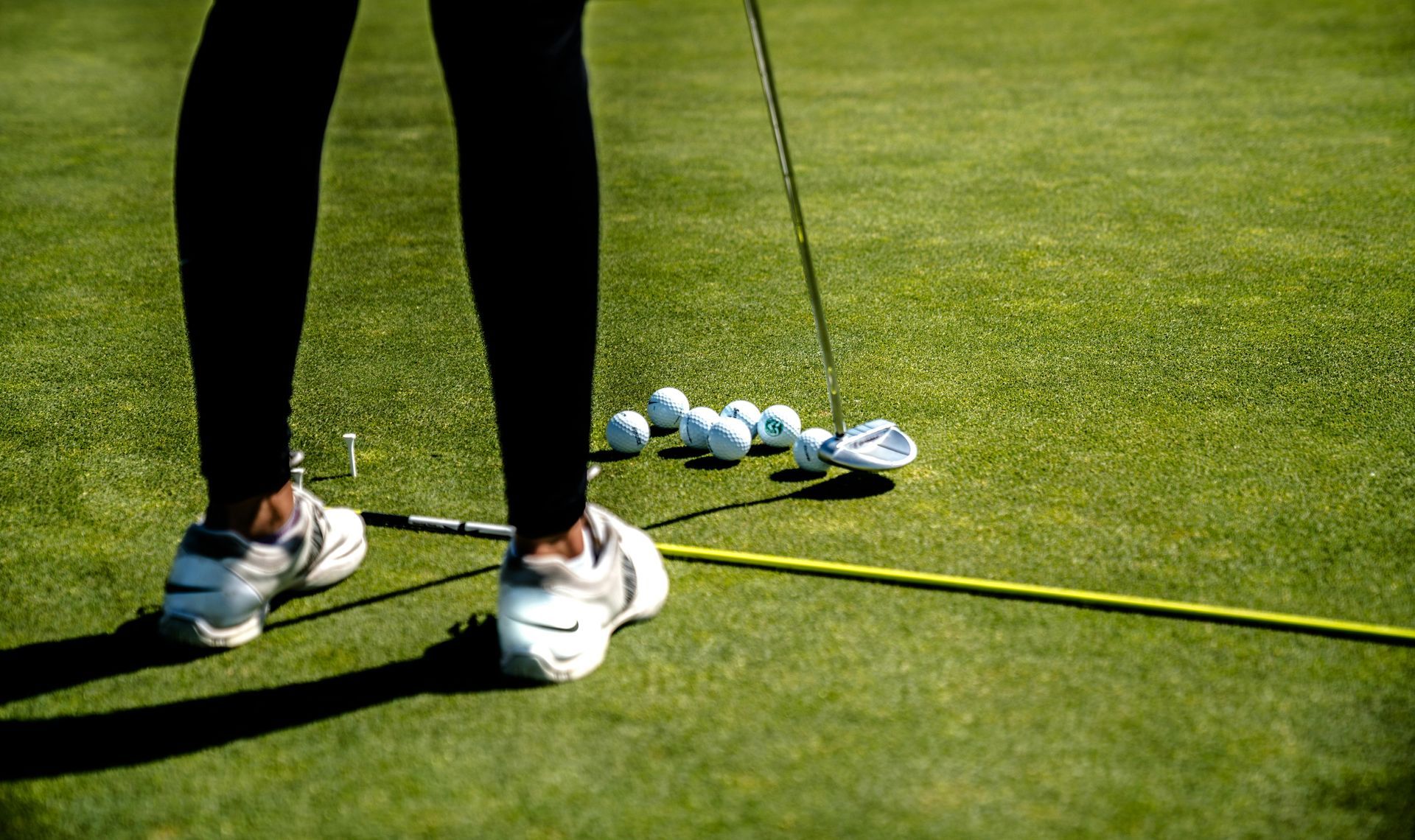 Beine eines Golfers neben einem Haufen Golfbälle auf dem Übungsgrün
