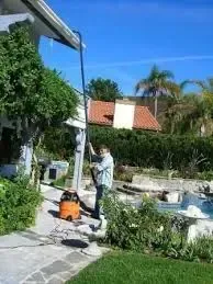 A man is cleaning the side of a house with a vacuum cleaner.