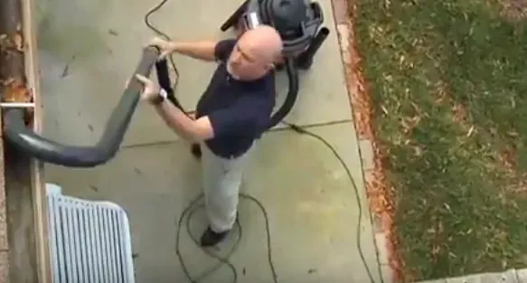 A man is using a vacuum cleaner to clean a gutter.