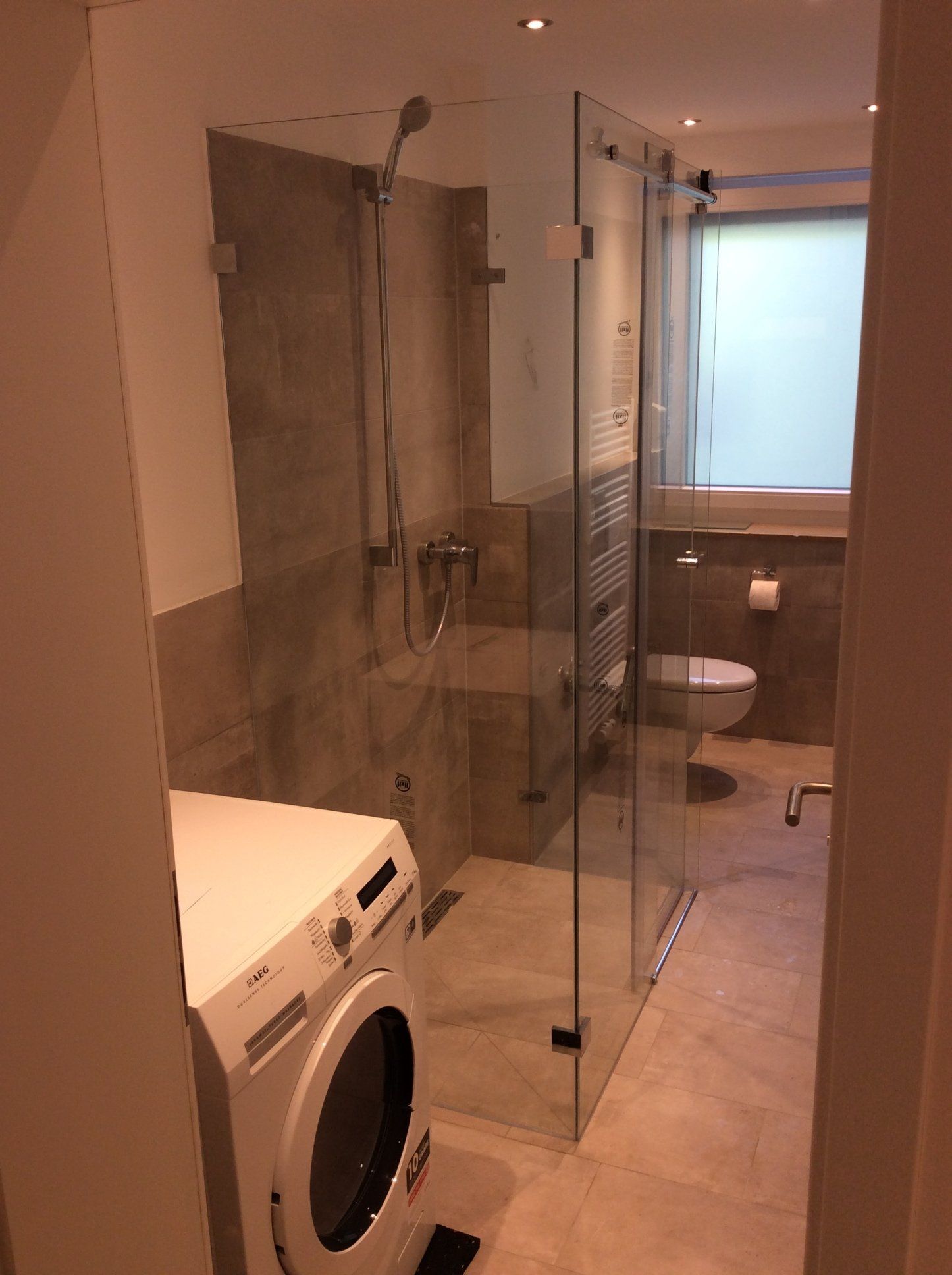 Schmale Glasdusche neben Waschmaschine