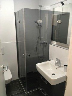 Dusche mit Eckeinstieg neben Waschtisch schwarze Wandfliesen